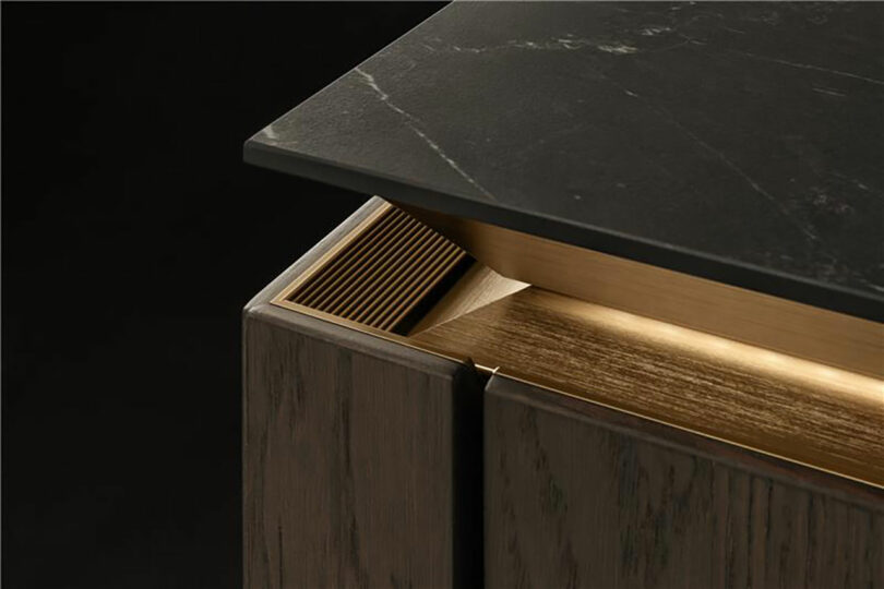 Close-up of a cabinet corner with a dark matte countertop, wood grain finish, and metallic gold accent detailing.