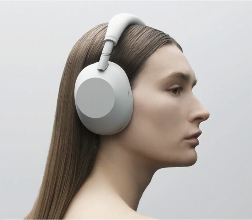 Person with long straight hair wearing WH-1000XM6 over-ear wireless headphones, shown in profile against a plain light background.