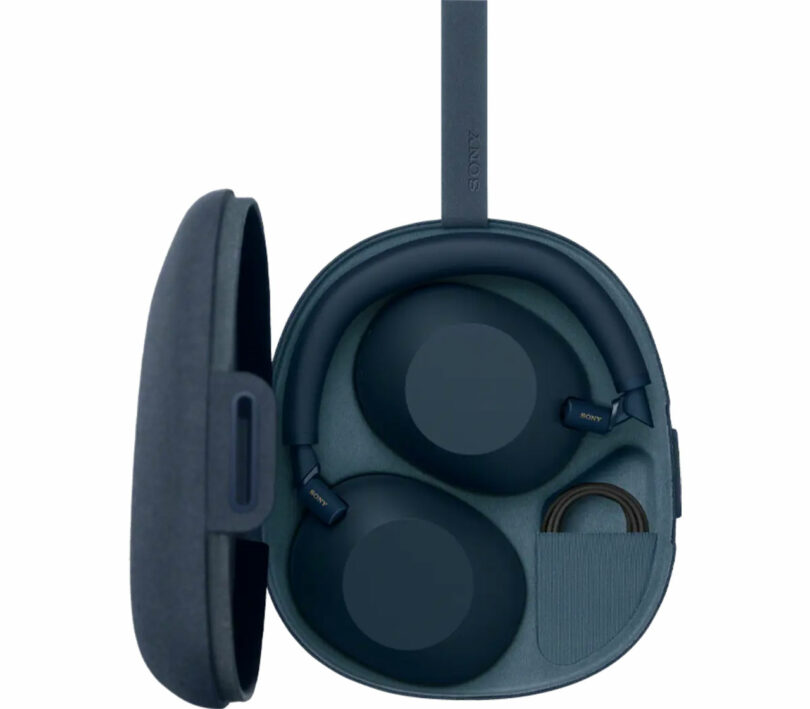 A pair of black over-ear Sony WH-1000XM6 headphones rests inside an open hard carrying case, with a storage compartment holding a coiled cable.