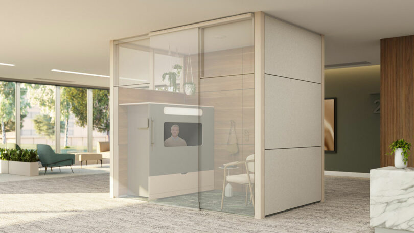 A modern office privacy pod with glass walls offers an Ocular View of the workspace, featuring a small table, chair, and monitor inside, all situated in an open, well-lit environment.