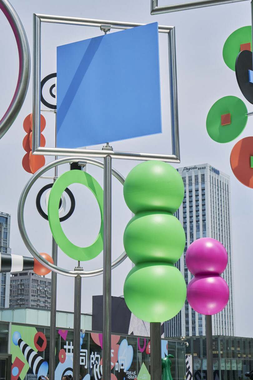Colorful abstract outdoor sculptures featuring geometric shapes and spheres, with tall buildings and signs visible in the background.