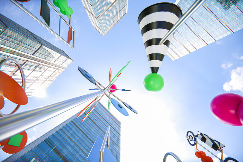 View looking up at tall modern buildings and colorful abstract sculptures against a bright blue sky.
