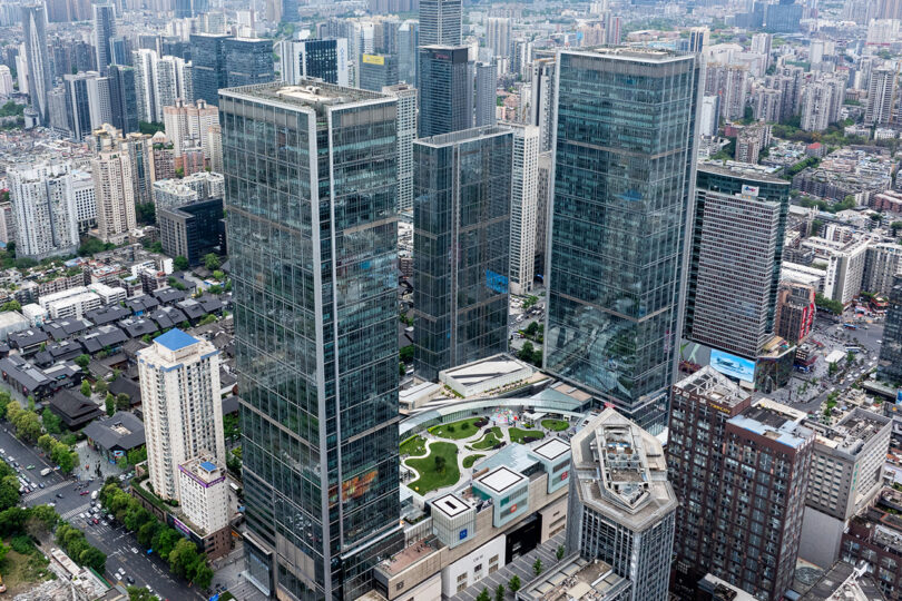 Aerial view of modern high-rise office buildings and an urban park surrounded by city streets and dense developments.