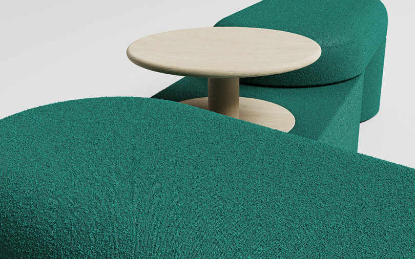 Curved teal upholstered seating with a light wood round side table placed between the seat sections, on a white background.