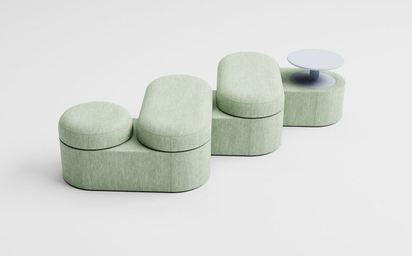 A modular green upholstered seating unit with three rounded seats at different heights and an integrated small round white side table.
