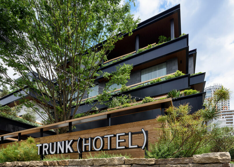 A modern hotel building with multi -storey, with stratified balconies and greenery, with a reading sign "Trunk (hotel)" in the foreground.