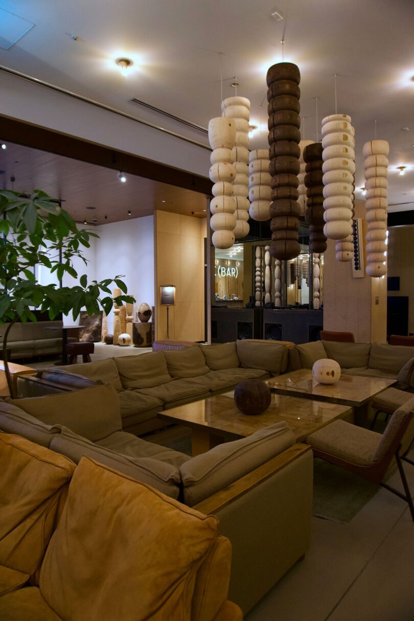 Modern hotel lounge with beige sofas, a large wooden coffee table, decorative hanging wooden sculptures, and. a potted plant at TRUNK(HOTEL) CAT STREET.