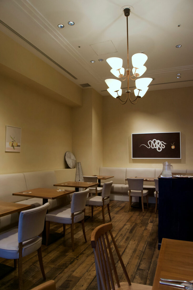 A minimalist restaurant dining area at TRUNK(HOTEL) CAT STREET features wooden floors, light-colored walls, simple tables and chairs, and modern artwork on the walls