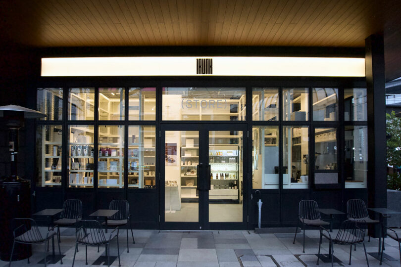 A modern storefront at TRUNK(HOTEL) CAT STREET called TRUNK(STORE) with large glass windows and doors, minimalist black-framed seating outside, and shelves with products visible inside.
