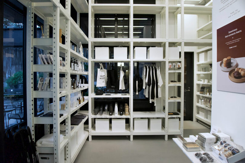 A minimalist retail store interior at TRUNK(HOTEL) CAT STREET features white shelves displaying neatly organized clothing, books, and lifestyle products; large windows provide natural light