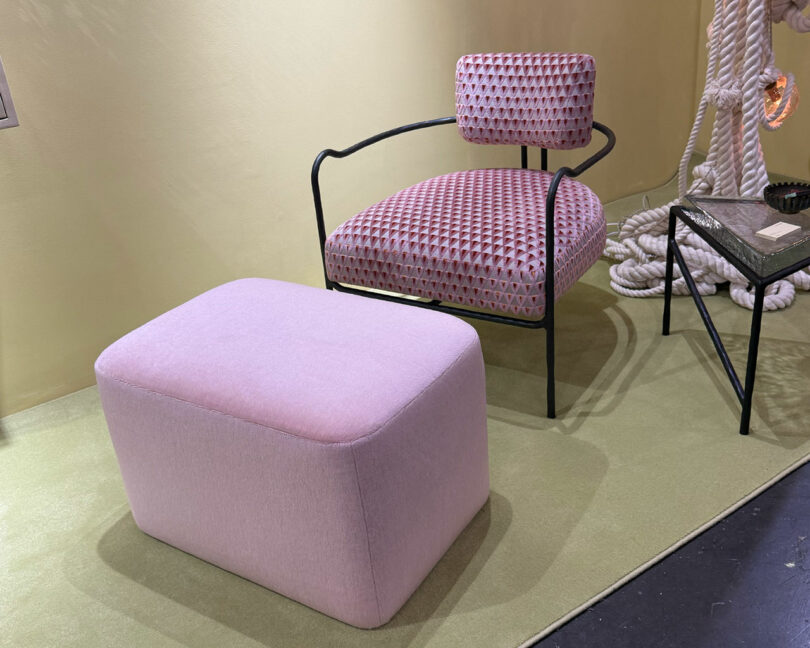 A pink upholstered armchair with a geometric pattern and black frame sits next to a matching pink ottoman on a light green rug—perfect inspiration for your Wanted Design 2025 decor. A black side table and rope decor are nearby.