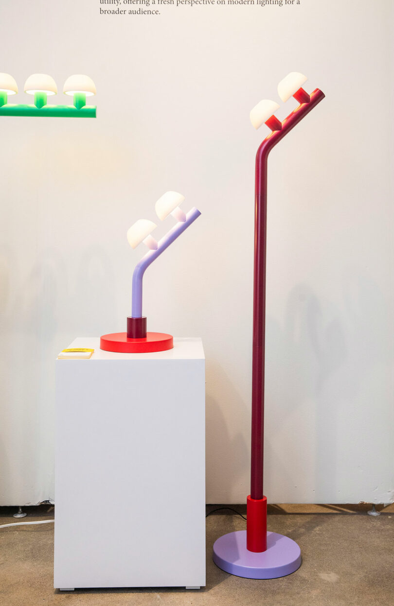 Two modern Nader Gammas lamps with colorful bases and three bulb-like lights each are displayed; one table lamp is on a pedestal, while the striking floor lamp stands elegantly on the ground.
