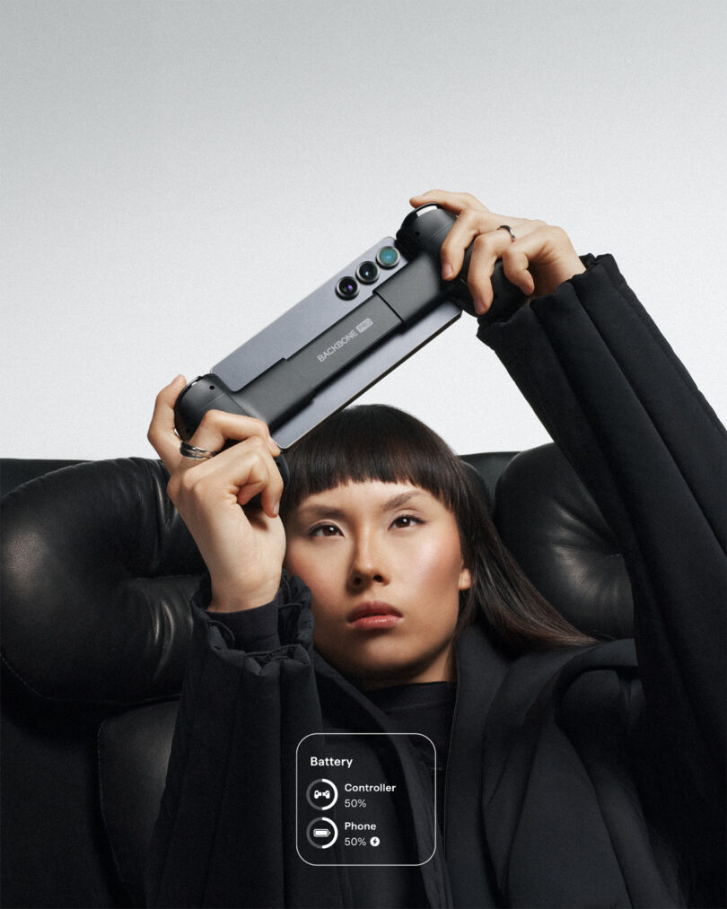 A person sits on a black leather chair holding a Backbone One gaming controller with a phone attached; battery status for controller and phone is displayed.