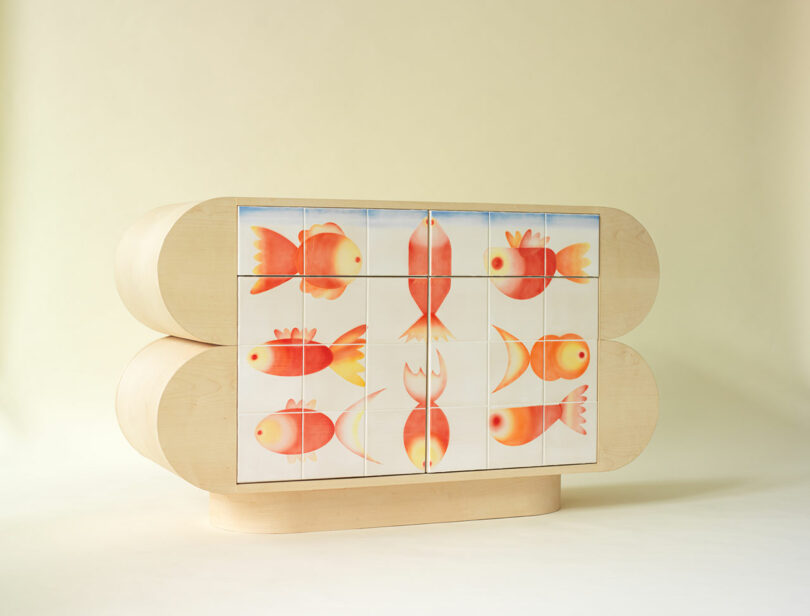 A light wood cabinet with rounded edges features a front decorated with colorful, abstract fish illustrations arranged in a grid pattern.
