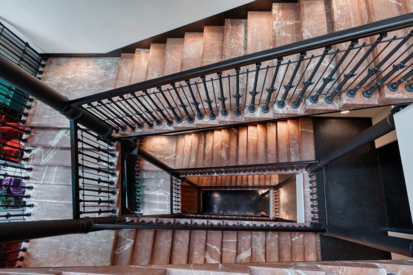 A top-down view of a multi-level staircase with brown marble steps and black metal railings in a well-lit interior.