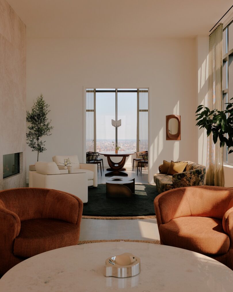Bright living room with modern furniture, large windows, neutral walls, two rust-colored chairs, a round table, and cityscape view in the background.