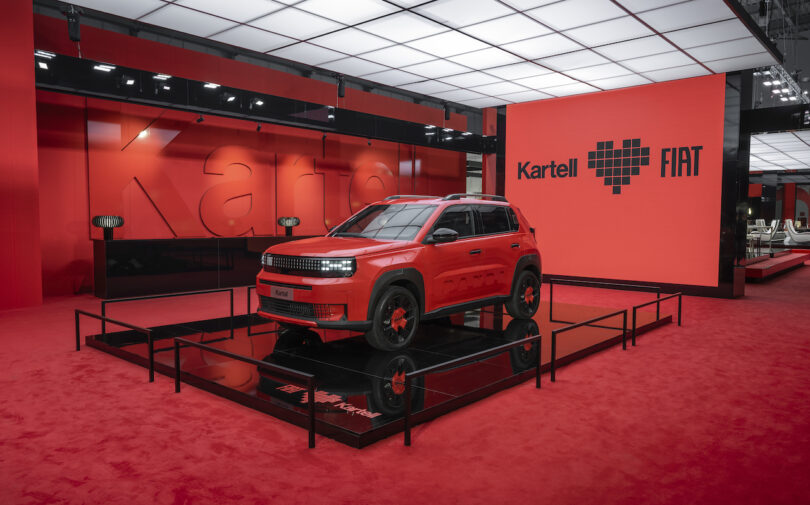A red Fiat SUV is displayed on a raised platform in a showroom with red walls and flooring, featuring "Kartell ♥ FIAT" signage in the background