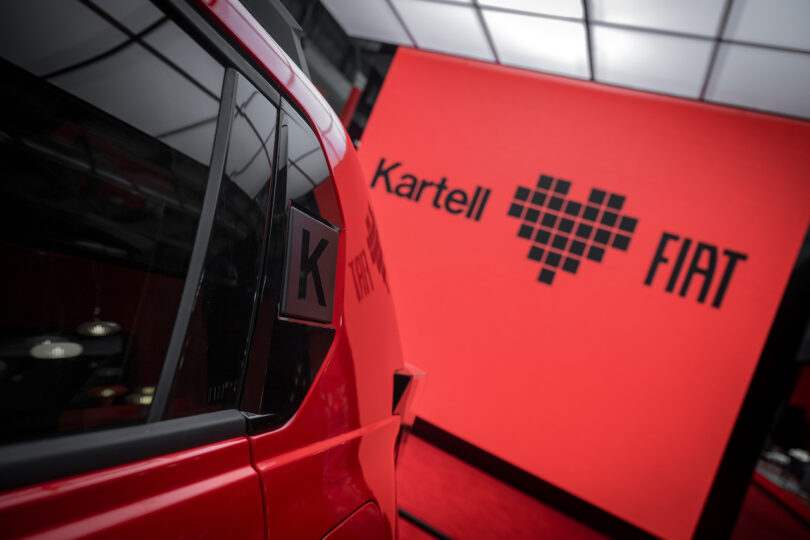 Close-up of a red vehicle next to a large red display panel with the Kartell and FIAT logos, including a pixelated heart symbol between them