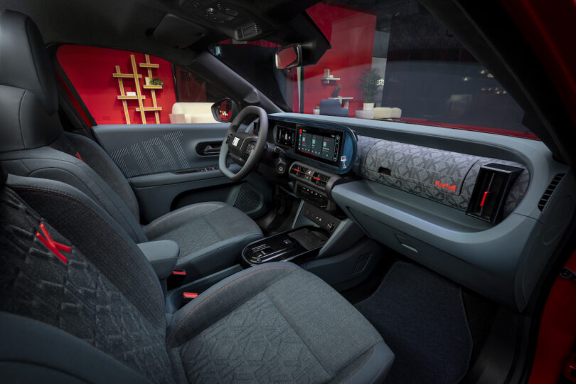 Modern car interior with patterned fabric seats, digital dashboard, and infotainment screen, featuring red accents and a sleek, minimalist design