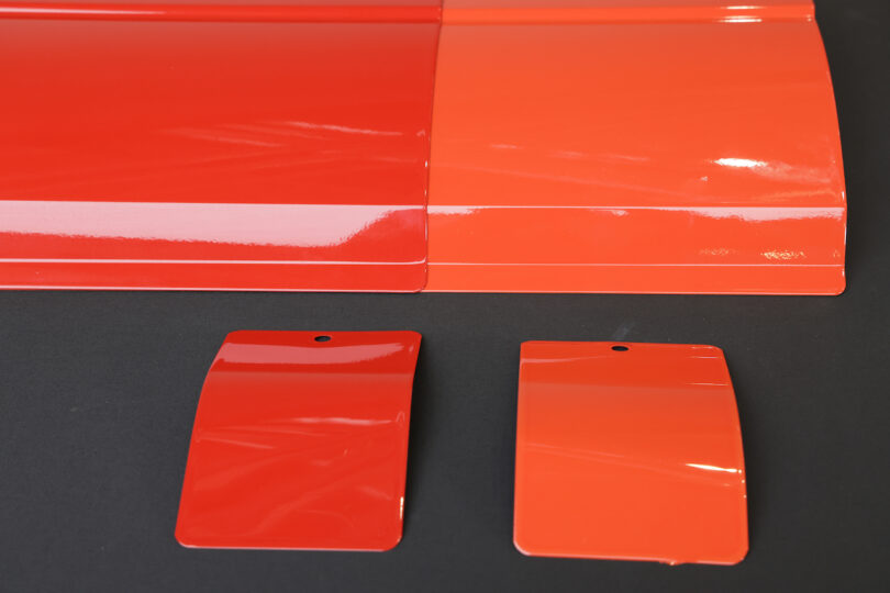 Four glossy red and orange color samples are displayed on a black surface, with two larger panels above and two smaller, rectangular swatches below