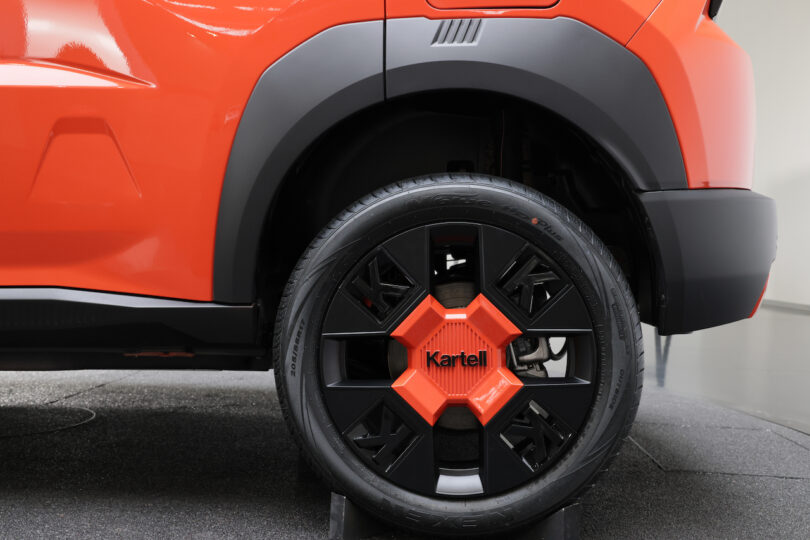 Close-up of the rear wheel and fender of an orange vehicle, featuring a black and orange rim with the word "Kartell" on the center cap