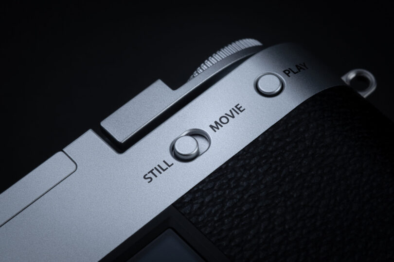 Close-up of a camera mode dial with options labeled "STILL," "MOVIE," and "PLAY" on a metallic and black textured surface.