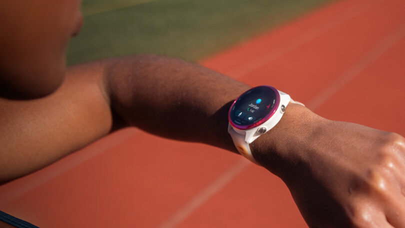 Person checking a Garmin smartwatch displaying a running activity on a track.