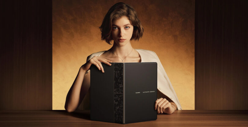 A woman with short hair sits at a table holding an open laptop with the words "Huawei MateBook" visible on the cover. The background is a warm, brown gradient.