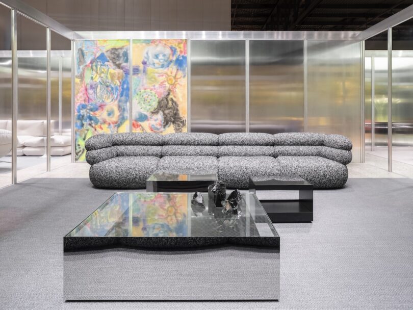 A modern living room with a textured gray sofa, mirrored coffee table, abstract wall art, and metallic walls