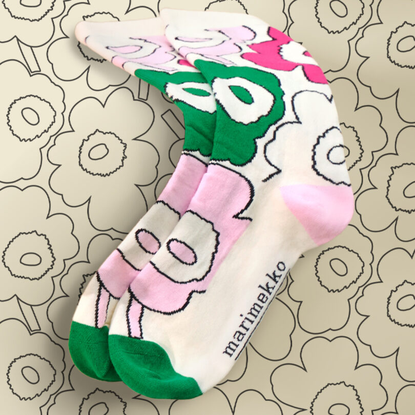 A pair of socks with pink, green, and white floral patterns and the word "marimekko" on the side, placed on a background with similar flower designs