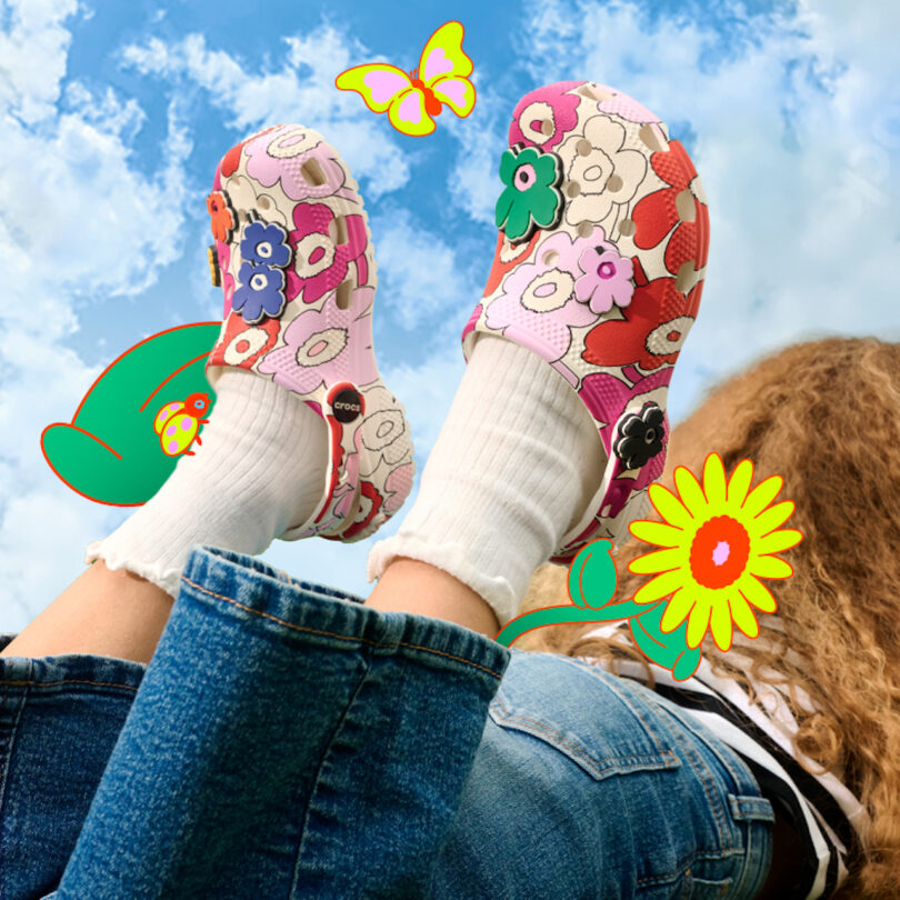 Person in blue jeans and white socks wears floral-patterned clogs, with illustrated flowers and a butterfly against a blue sky background