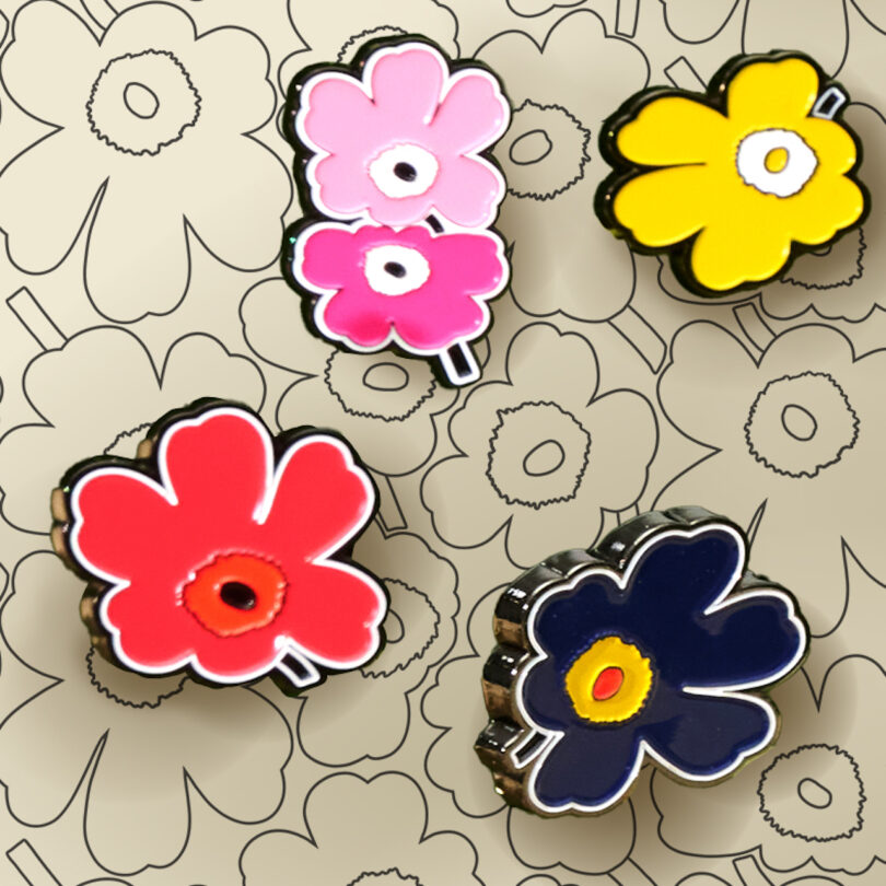 Four colorful floral charms—pink, yellow, red, and navy—are arranged on a beige surface with a matching floral pattern background