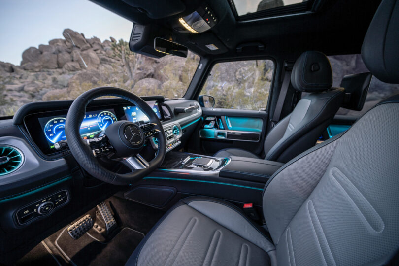 Interior view of the luxury G580 SUV featuring a Mercedes-Benz logo, digital displays, leather seats, and a panoramic sunroof with rocky terrain visible through the windows.