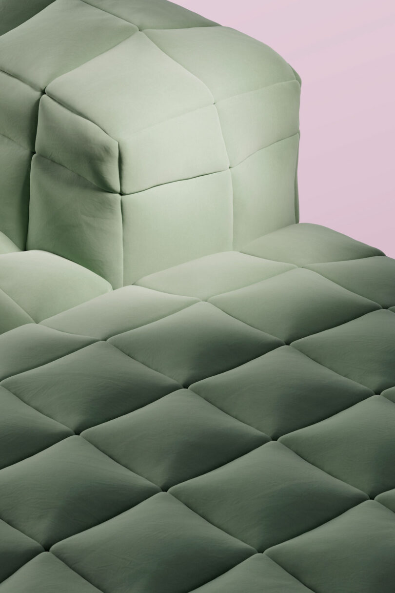 Close-up of a quilted surface with a soft, cushioned texture in a muted green color, set against a pale pink background.