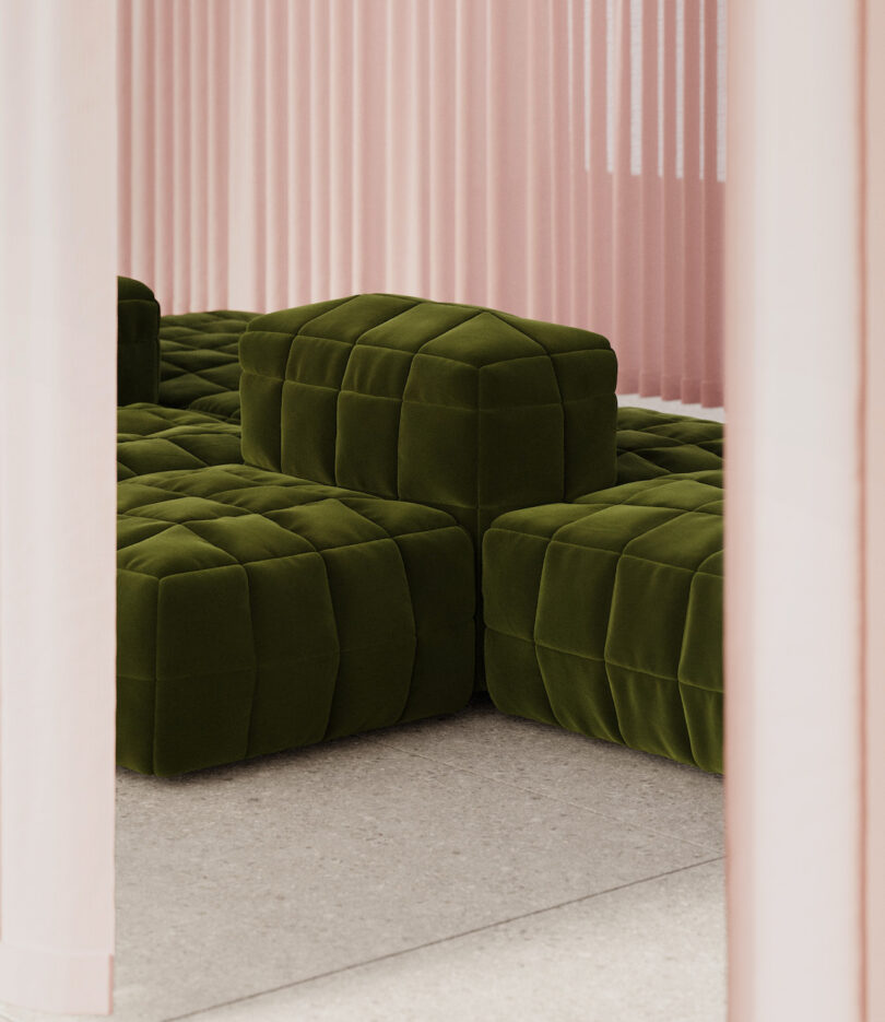 Olive green, tufted modular seating is arranged on a light floor, framed by pale pink vertical blinds