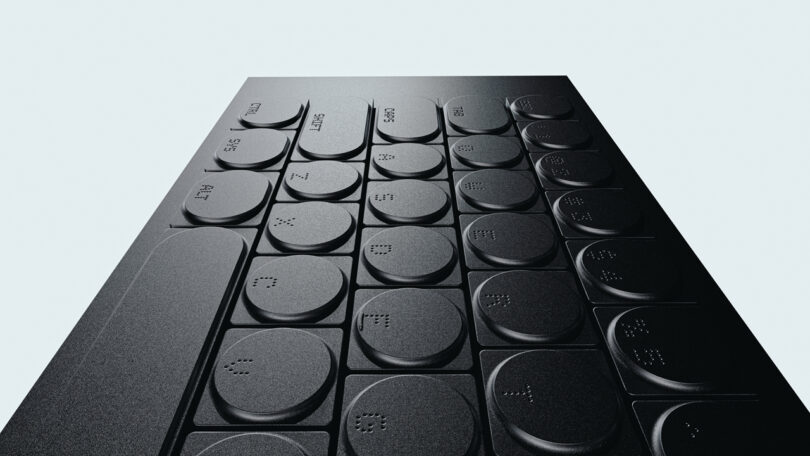Close-up view of a sleek black computer keyboard with rounded keys, some featuring raised braille dots for accessibility—a cleaver design blending style and functionality.