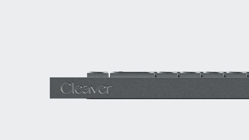 A close-up side view of the minimalist Cleaver keyboard in dark gray, with "Cleaver" elegantly engraved on its edge, set against a plain white background.
