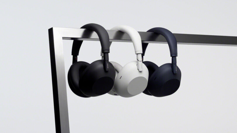 Three pairs of WH-1000XM6 over-ear headphones in black, white, and navy hang side by side on a metal bar against a plain background.
