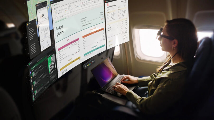 A person on an airplane uses a laptop and augmented reality glasses to view multiple virtual screens with documents and applications.