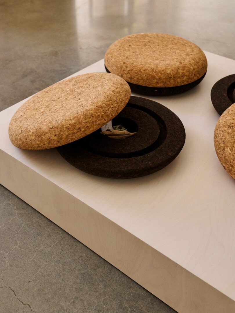 Three large, round cork lids rest on dark circular bases atop a white platform; one lid is partially open, revealing an interior compartment.