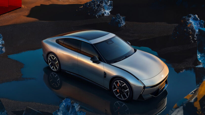 A sleek silver XPeng P7 electric sports sedan is parked on a reflective surface surrounded by rocky terrain under dramatic lighting.