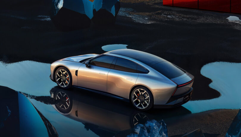 A sleek silver XPeng P7 sports car is parked on a wet, reflective surface with futuristic, angular structures in the background.