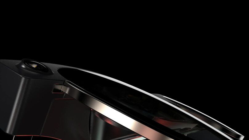 Close-up of a sleek, modern black and metallic appliance or device with a curved glass surface, set against a plain black background.