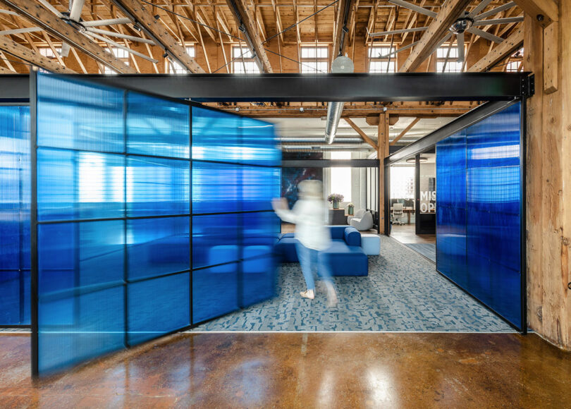 A person walks quickly past blue translucent partition walls in a modern office space with exposed wooden beams and industrial design elements, evoking the innovative spirit of Astroscale.