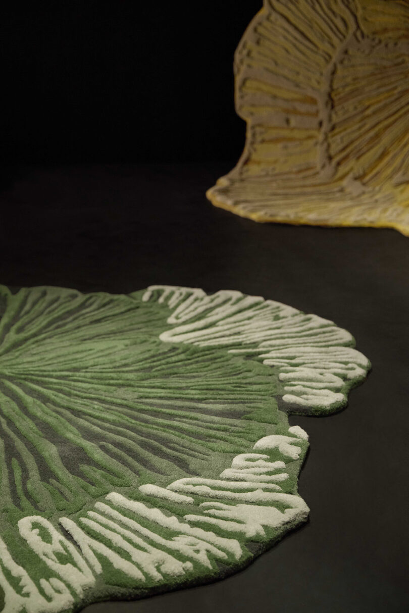Two rugs shaped and patterned like the cross-sections of mushrooms, one green and white in the foreground and one yellow and white in the background, on a dark surface.
