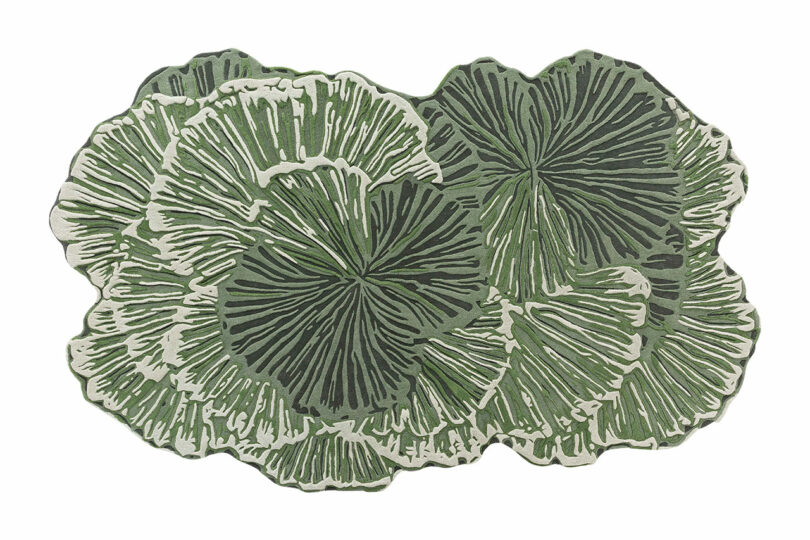 A decorative rug featuring an abstract pattern of overlapping green and white shapes resembling large leaves or coral, inspired by the Botanica Bodo Sperlein collection.