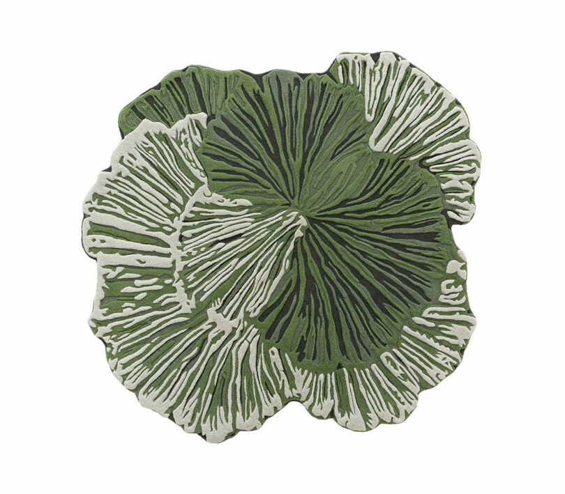A green, leaf-shaped rug from Botanica Bodo Sperlein with white and dark green vein patterns, resembling overlapping leaves or plant forms, on a white background.