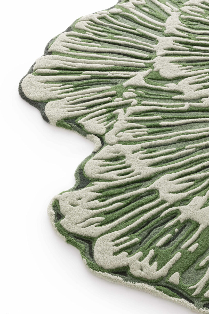 A close-up of a textured, irregularly shaped rug from the Botanica Bodo Sperlein collection, featuring green and off-white organic patterns resembling plant leaves or growth rings.