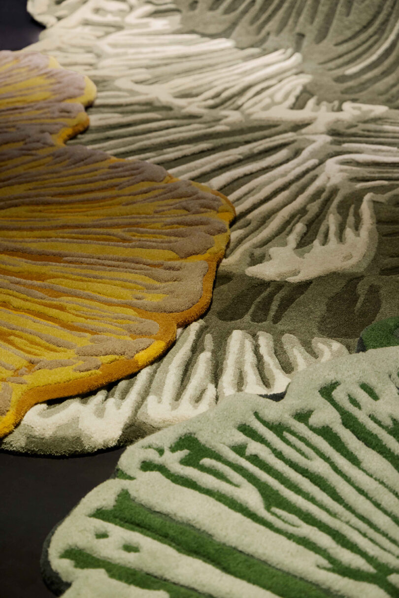 Close-up of a textured area rug with overlapping leaf-like shapes in yellow, green, and shades of beige, featuring raised patterns and organic edges.