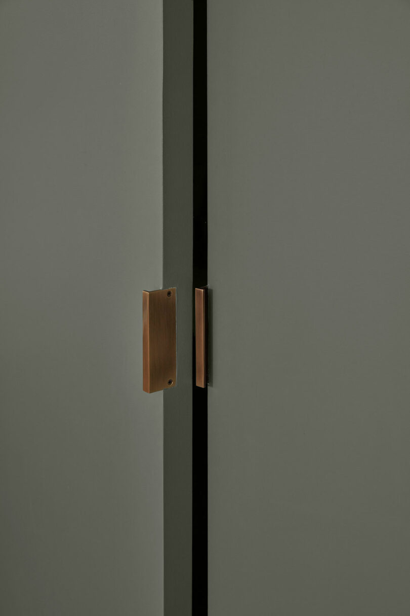Minimalist close-up of two matte gray doors with brass vertical handles and a central black gap between them.